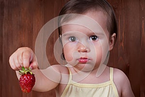 Cute upset little girl is holding the big ripe strawberry