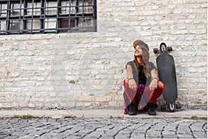 Cute urban girl with longboard sitting sitting next to a brick wall