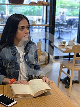 Cute, urban girl sitting in cafe, reading  a book