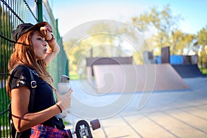 Cute urban girl with skateboard drinking water on a hot day