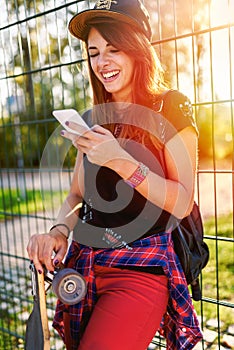 Cute urban girl in skatepark with skateboard using smart phone