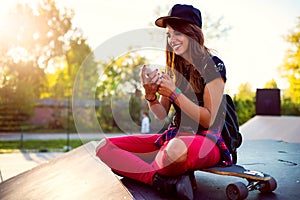 Cute urban girl in skatepark with skateboard using smart phone