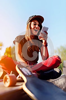 Cute urban girl in skatepark with skateboard using smart phone