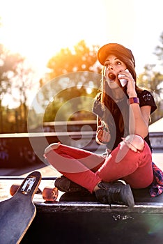 Cute urban girl in skatepark with skateboard using smart phone