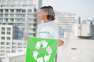 Cute volunteer woman holding recycling sign looking away