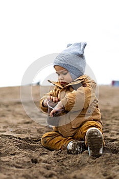 Cute warm weared little baby boy playing in a sand on the winter beach