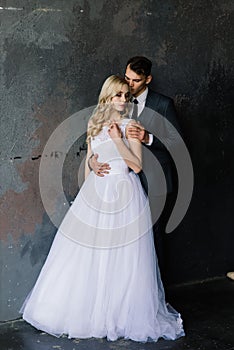 Cute wedding couple in interior of classic studio. They kiss and hug each other.