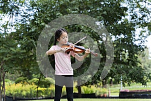 A cute white Asian girl is playing the violin in the middle of beautiful nature, greenery and sunlight