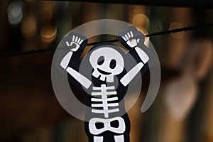 Cute White skeleton bone hanging by black rope with bokeh blurred background, halloween holiday festival