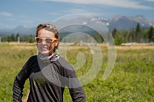 Cute, wholesome adult woman with braided hear poses in a meadow in Polebridge Montana. Neck gaiter face mask and smiling