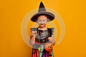 Cute witch kid girl with yummy marmalade jelly worm and Halloween pumpkin candy basket or Jack o Lantern bucket looking down on ye