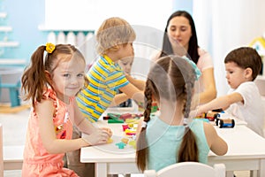 Cute woman and kids playing educational toys at kindergarten or nursery room