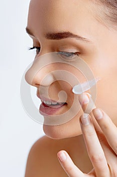 Cute woman applying cream to her face. Closeup up of a young woman applying beauty product