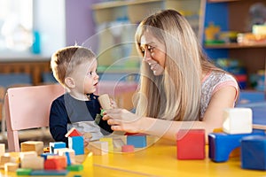 Cute woman and baby boy playing educational toys at creche or nursery