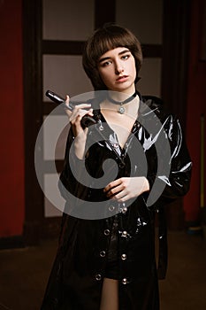 Cute woman in a black raincoat with a gun in her hand with a short haircut