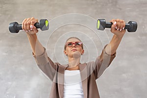 Cute woman in casual clothing holds two dumbbells in hands and looking forward. Selective focus