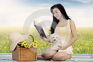 Cute woman and dog read book at field