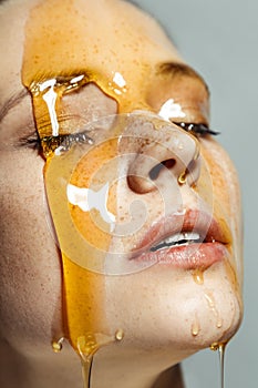 Cute woman with freckles and honey on face, with closed eyes, being satisfied of cosmetic procedures
