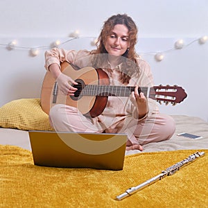 Cute woman guitarist plays a musical instrument. Online learning, music lessons guitar via laptop