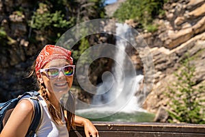 Cute woman hiker with braided hair wearing a tank top poses at Running Eagle Falls waterfall in Glacier National Park