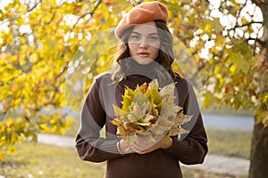 Cute woman holding autumn leaves in the nature. Fall foliage. Outdoor fun in autumn.