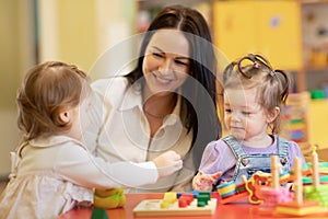 Cute woman and kids playing educational toys at kindergarten or nursery room