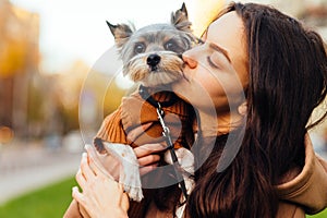 Cute woman kissing a cute little dog, close up portrait. Lady hugs a biewer terrier dog on the street. Love of woman owner and pet