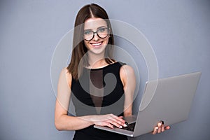 Cute woman with laptop standing over gray background