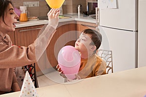 Cute woman playing with her son with balloons while having fun at the kitchen