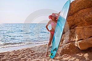 Cute woman posing with surfboard on seashore. Smiling girl in bright bikini on beach. Summer holidays and surfing idea