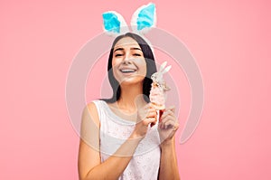 Cute woman in rabbit ears holding a rabbit toy, a traditional holiday, in the studio on a pink background