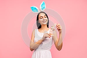 Cute woman in rabbit ears holding a rabbit toy, a traditional holiday, in the studio on a pink background, easter gift