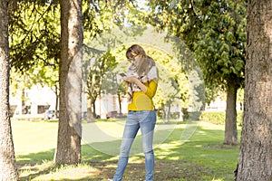 Cute woman is reading pleasant text message on mobile phone while taking a walk in the park in warm fall day