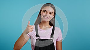 Cute woman showing thumb up sign over blue background. Positive young girl smiles to camera. Winner. Success. Body