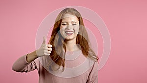 Cute woman showing thumb up sign over pink background. Positive young girl smiles to camera. Winner. Success. Body