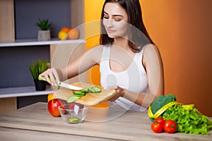 Cute woman slices cucumber for diet salad.