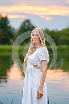 Cute woman standing by the river at sunset