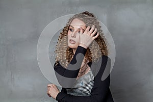 Cute woman touching her brown curly hair on gray background portrait