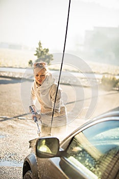 Cute woman washing her car in a manual carwash