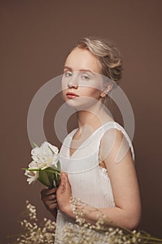 Cute woman in white shirt holding white flowers on brown background