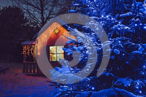 Cute wood play house in home garden, decorated with Christmas LED string lights outdoors.