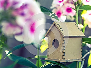 Cute wooden toy bird house in the blooming white pink phlox flowers against the green background