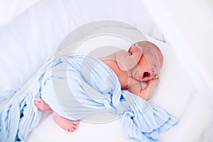 Cute yawning newborn baby in white bed