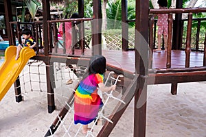 Cute 4 year old Asian girl is climbing rope net, a little kid clinging to the rope and clamber to the top. Bottom floor is a sand photo