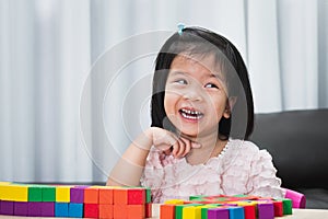 A cute 4-5 year old Asian girl is laughing at the imagination she creates playing with colorful wooden blocks.