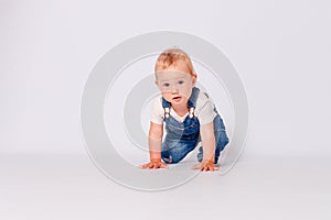 Cute year-old baby girl in a blue denim jumpsuit sits on white background. a child`s photo shoot