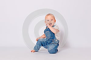 Cute year-old baby girl in a blue denim jumpsuit sits on white background. a child`s photo shoot