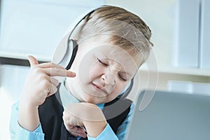 Cute 6 year old boy in suit listening to music or audio tutorial on headphones at the office background.