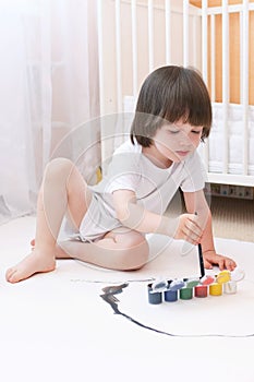 Cute 2 years boy with brush and gouache paints at home