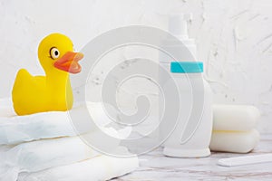 Cute yellow duckling sitting on diapers pile in the white bathroom. Baby hygiene. Daily care. Cleaning accessories